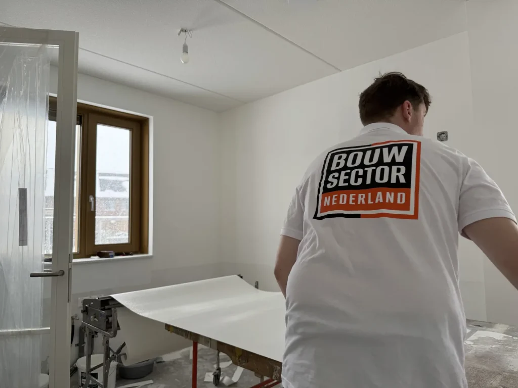 Behanger in wit poloshirt van Bouwsector Nederland rolt renovlies uit op de plaktafel