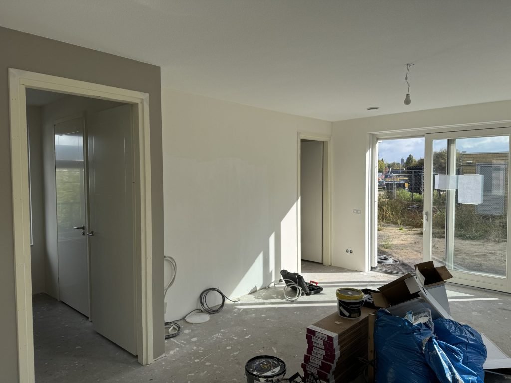 Kale woonkamer van een net opgeleverd huis met tuindeuren naar de bouwplaats