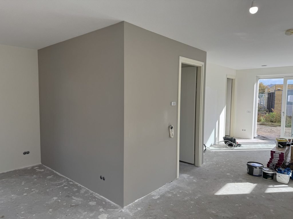 Woonkamer met een strak gesausde grijze wand rond de meterkast en een witte wand ernaast