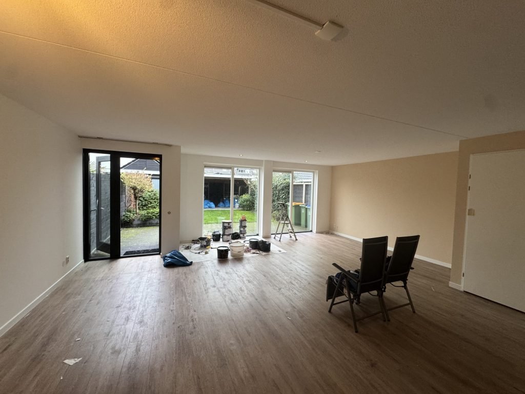Leeggemaakte woonkamer van een bestaande rijwoning met tuindeuren, klaar voor het behangwerk