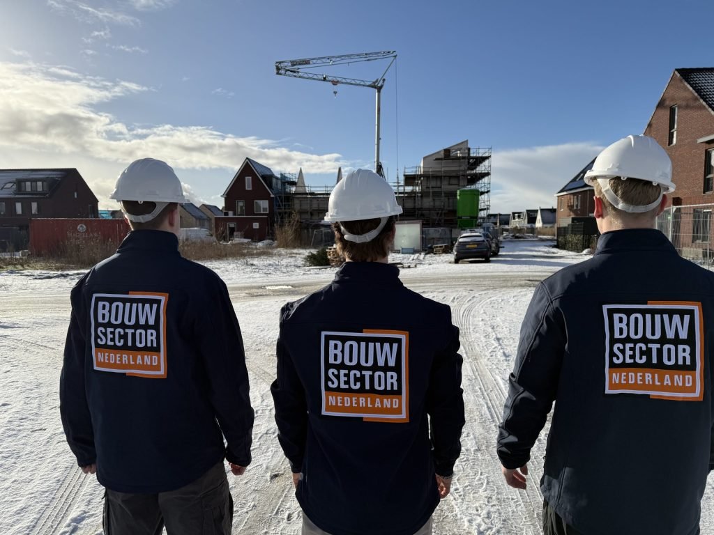Drie vakmensen van Bouwsector Nederland met witte helm op een winterse bouwplaats